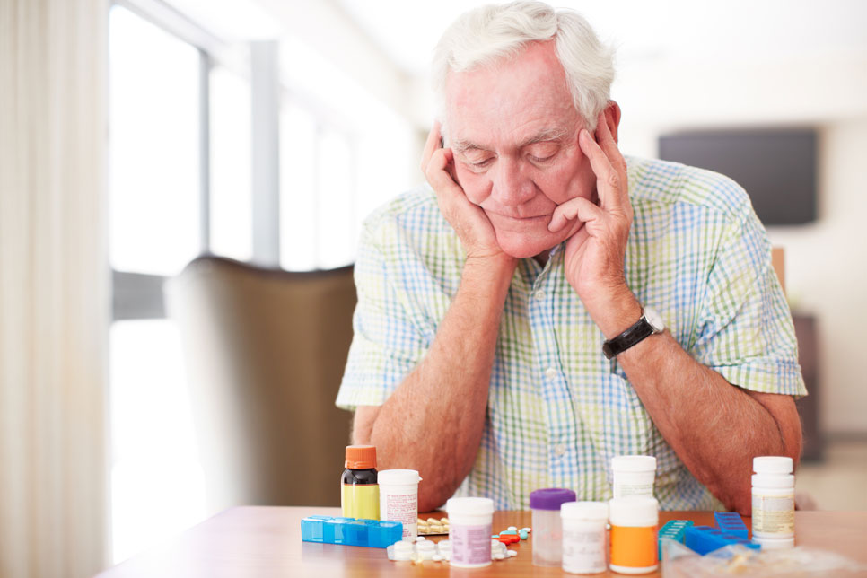 this is a image of a senior citizen looking frustrated at a lot of medication packaging